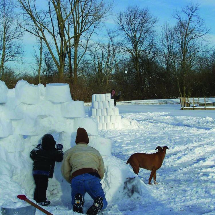 man and boy hiding behind wall of snow