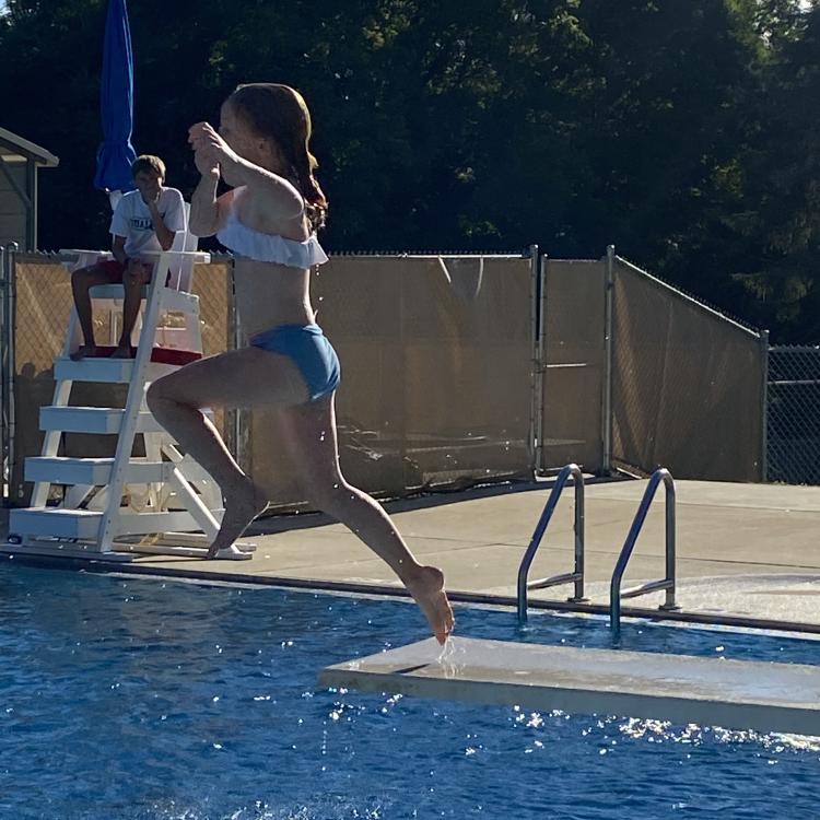 girl jumps off diving board into pool