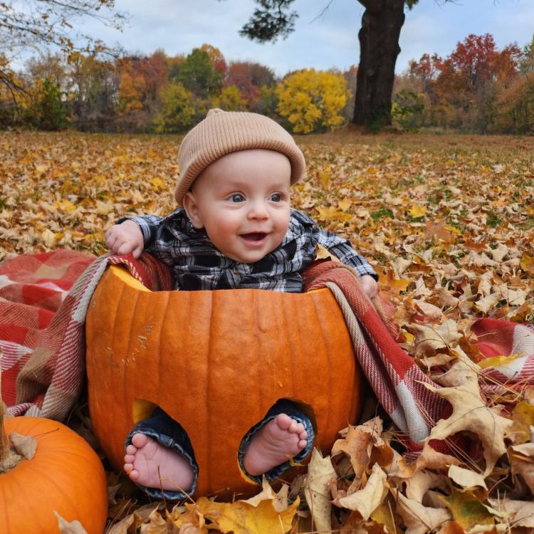 baby sitting in pumpkin among fall leaves