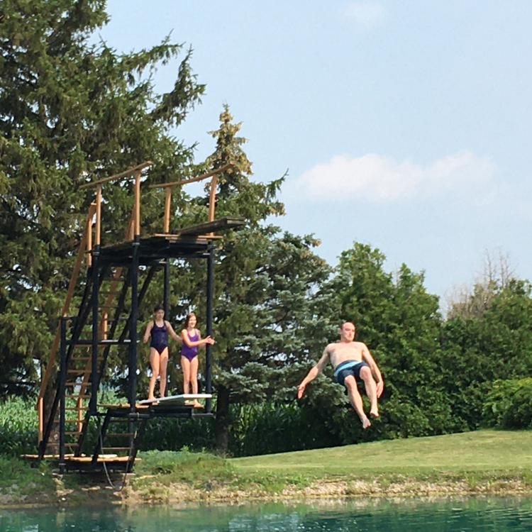 people jumping off diving board into pond