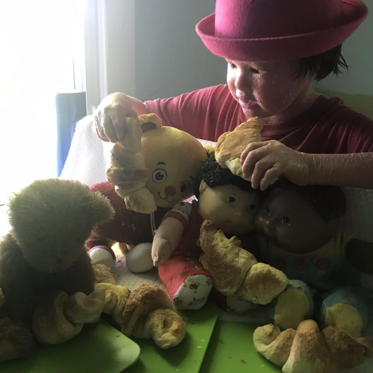 little boy in red hat shares croissants with teddy bears and dolls