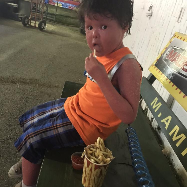 Small boy eating French fries on a bench.