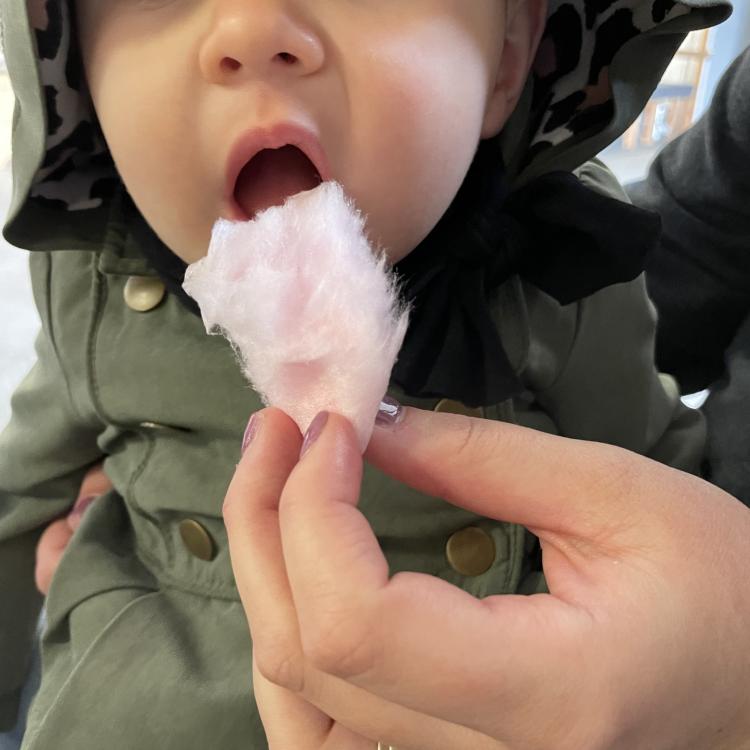 baby in overalls and hat opens up for a bite of pink cotton candy