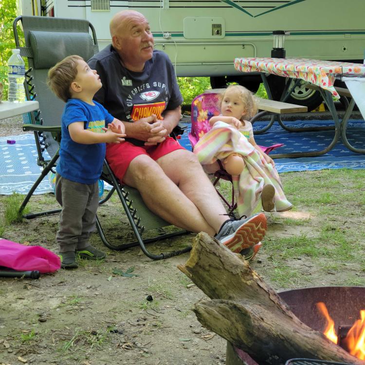 man and two small children looking upward behind campfire