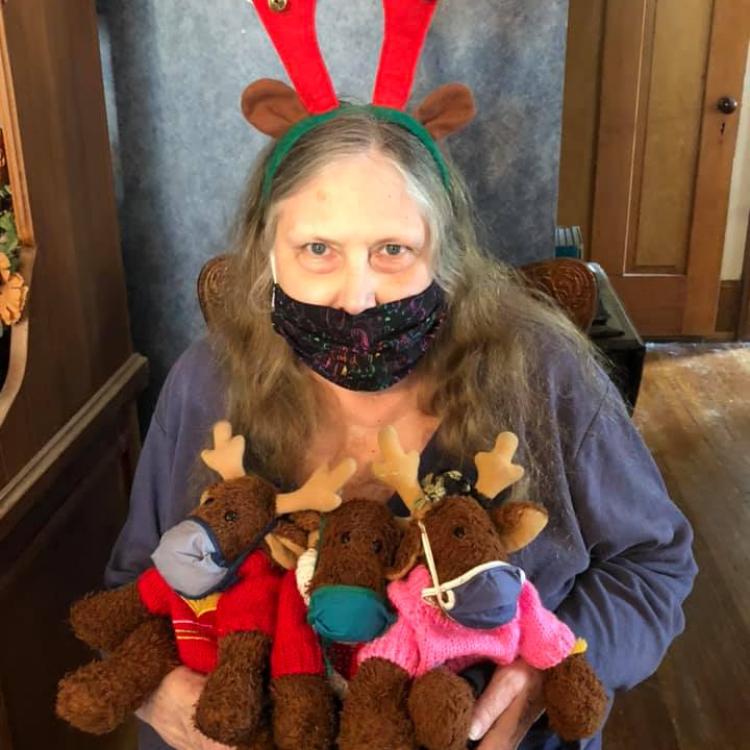 Woman wearing red antler headband, holding three stuffed reindeer