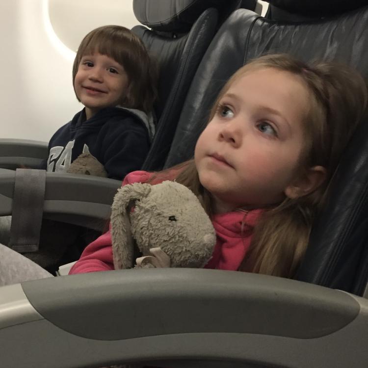 Small girl holding stuffed bunny in airplane seat with boy in next seat