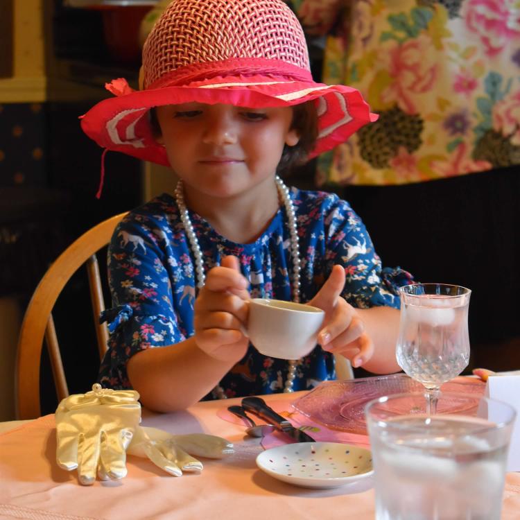 little girl with red hat and pearls, holding a teacup