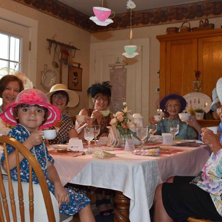 girl with red hat sits at table with women, all wearing festive hats