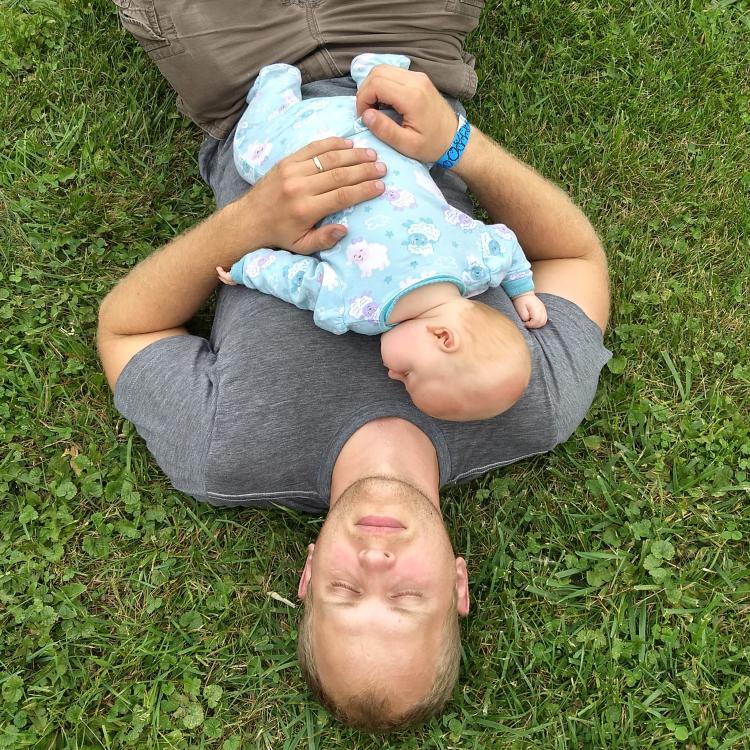 man sleeping on grass with baby on his chest