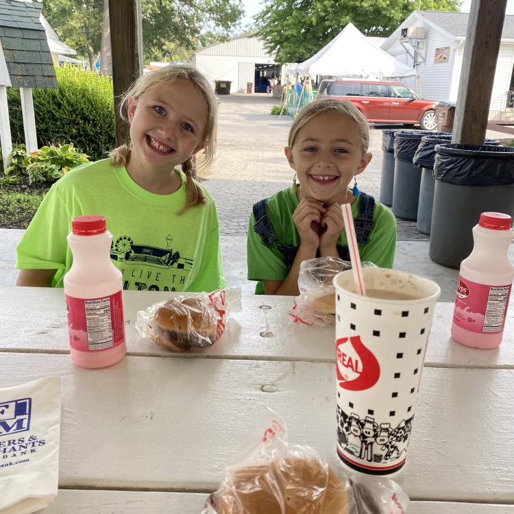 Two smiling girls behind table with food.