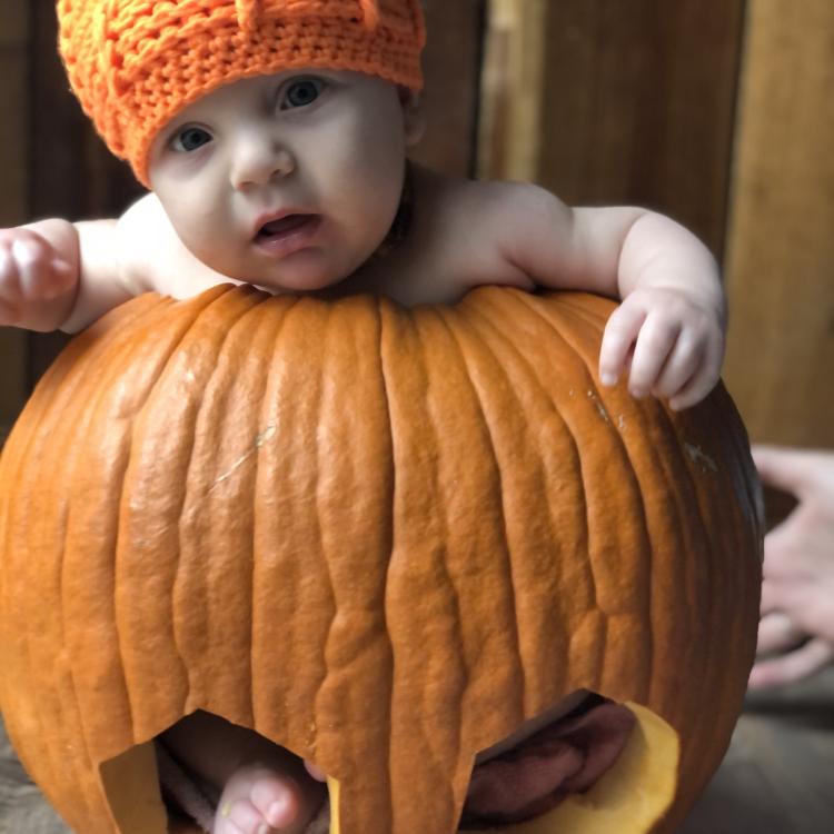 baby in a pumpkin hat sitting in a carved out pumpkin