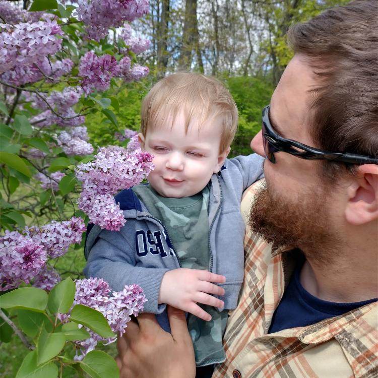 baby smelling lilacs on tree