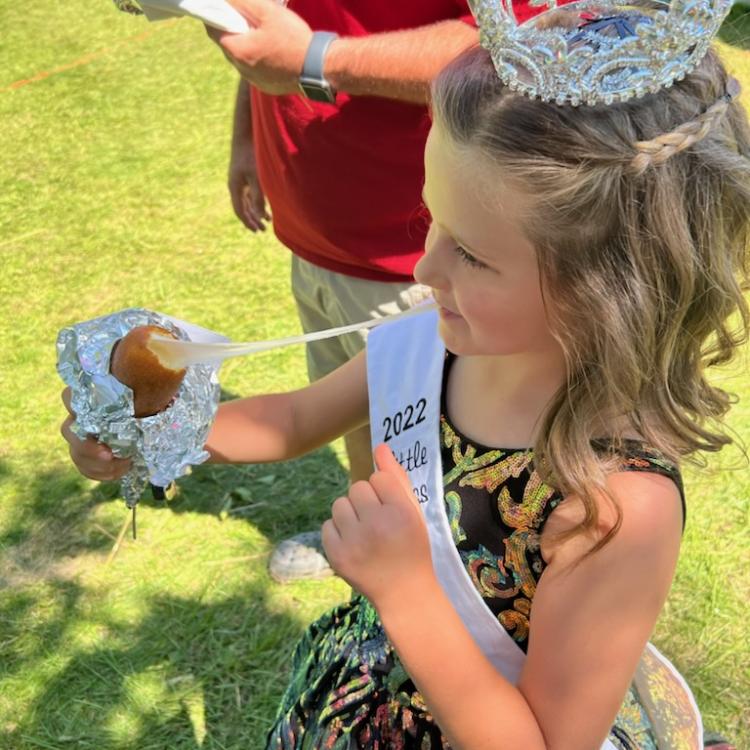 Little girl in crown and sash eating gooey fried cheese