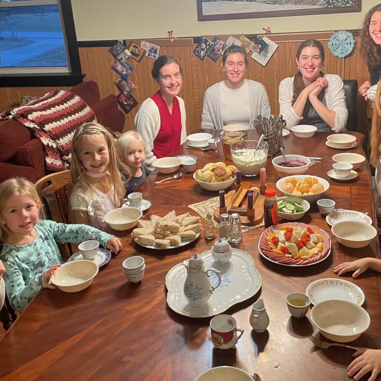 children and adults sit around a large table set for tea