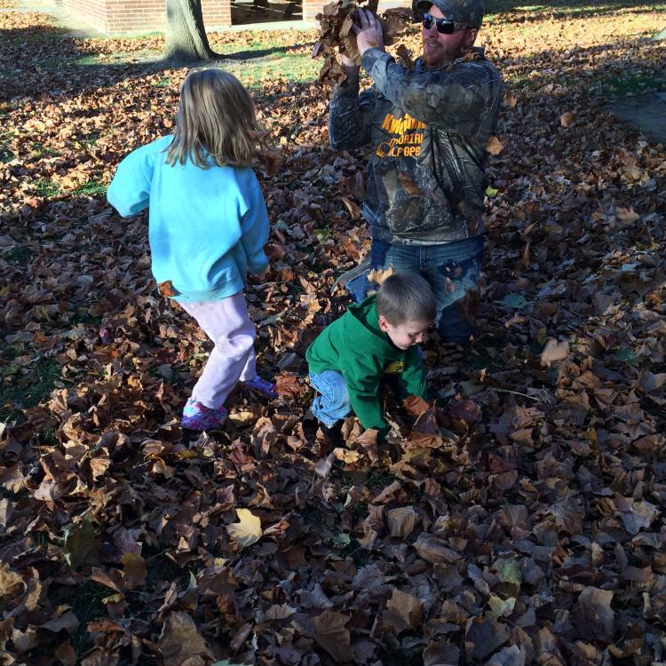 two children and a man toss leaves in leaf pile