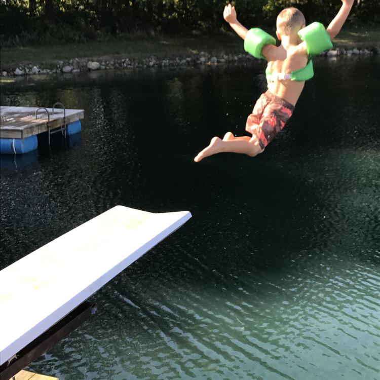 little boy leaps off board into lake