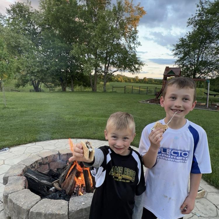 two boys in baseball uniforms eating s'mores by fire