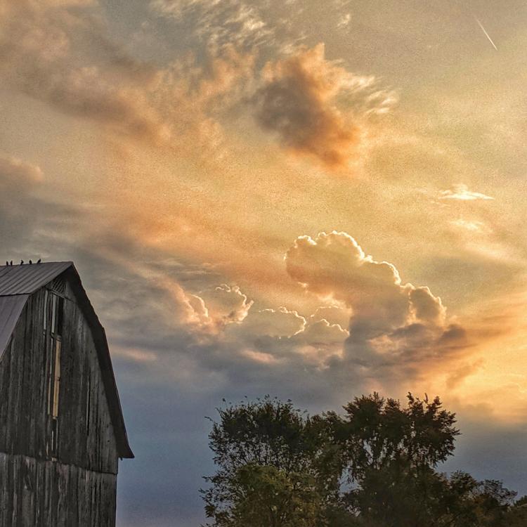 Tall brown wood barn with clouds and morning sun in background