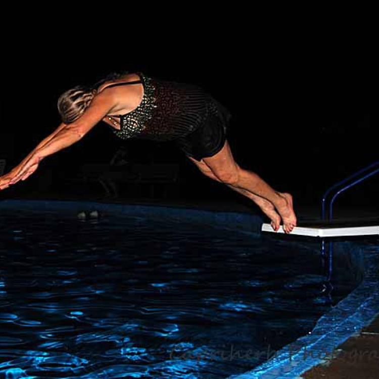 woman dives off board into pool at night