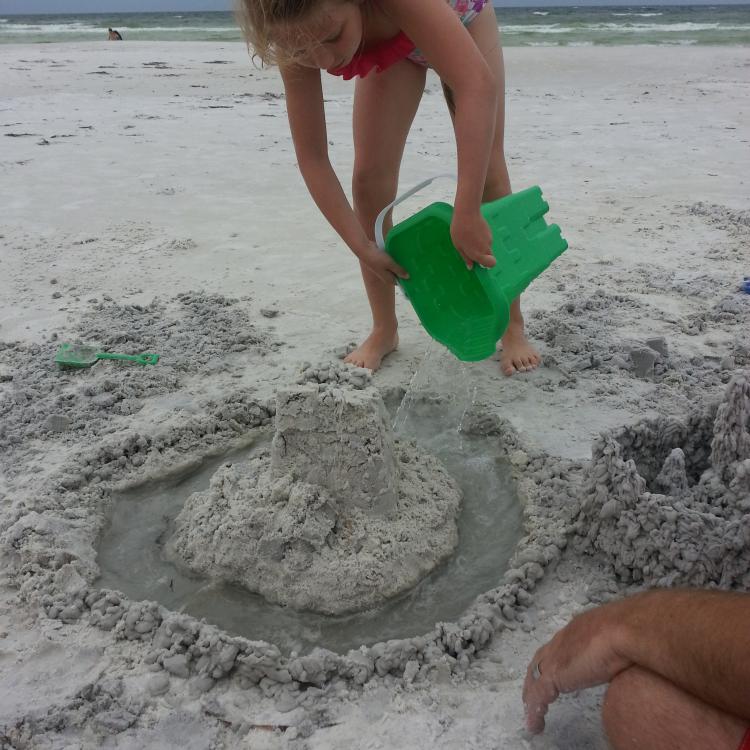 girl adds water to sandcastle moat