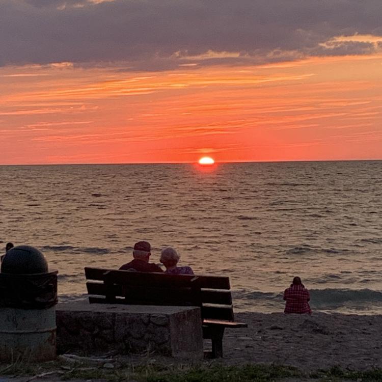 couple sits on bench watching sunset 