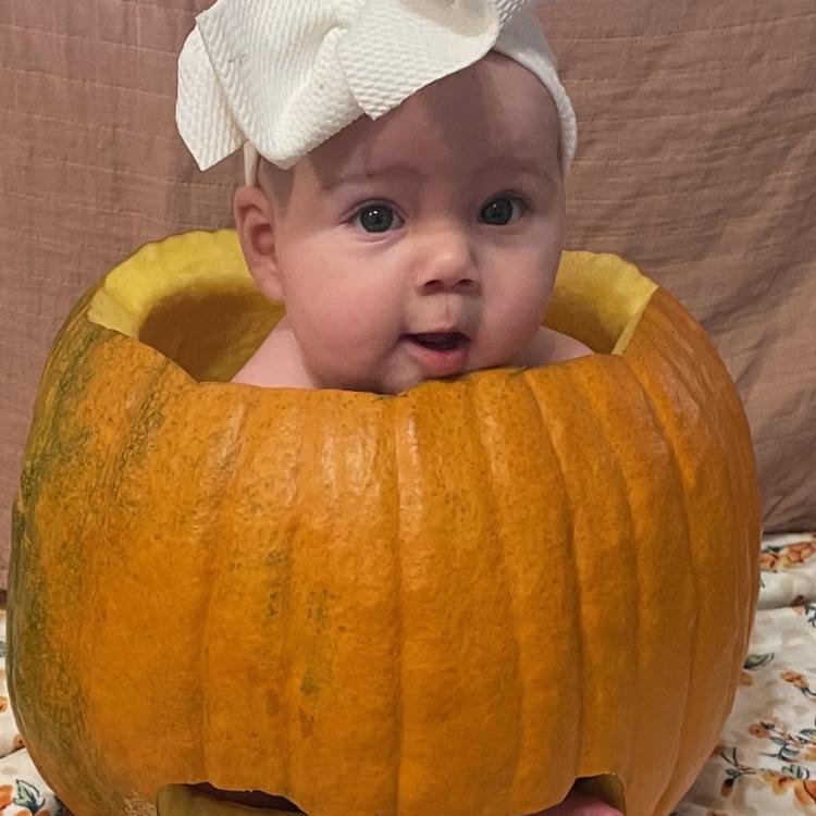 baby girl sitting in carved out pumpkin