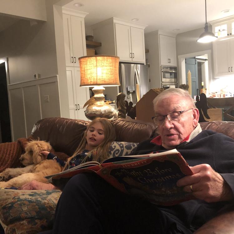 Man reading to girl, with dog on couch