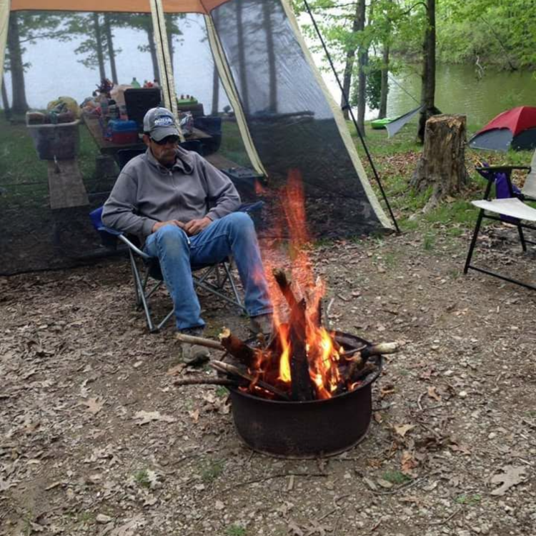 man in hat and sunglasses sitting by fire