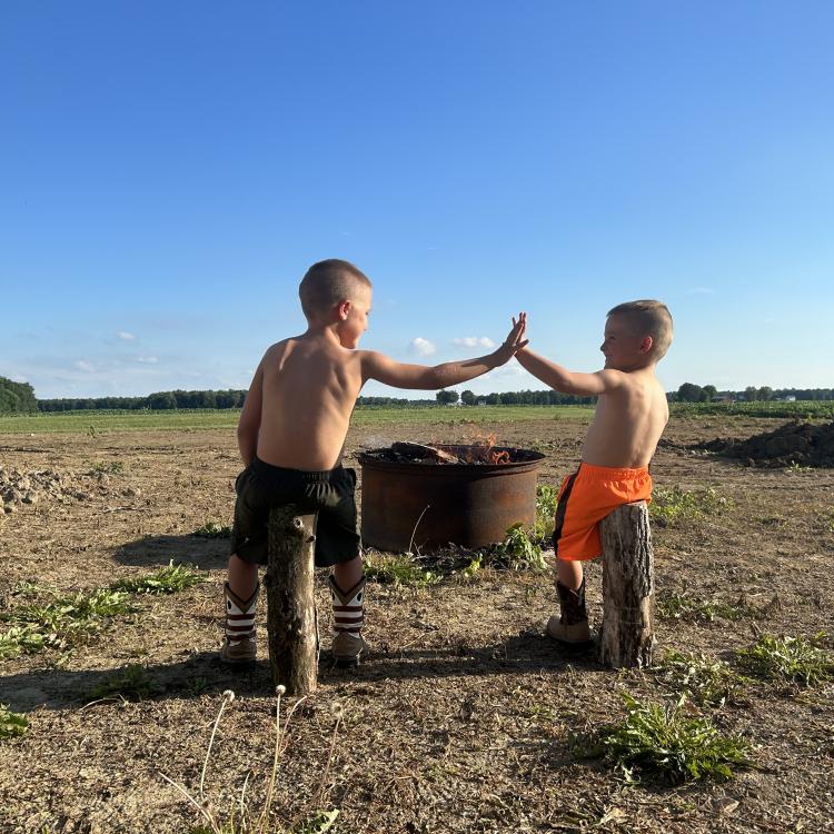 two boys give a high five in front of a campfire