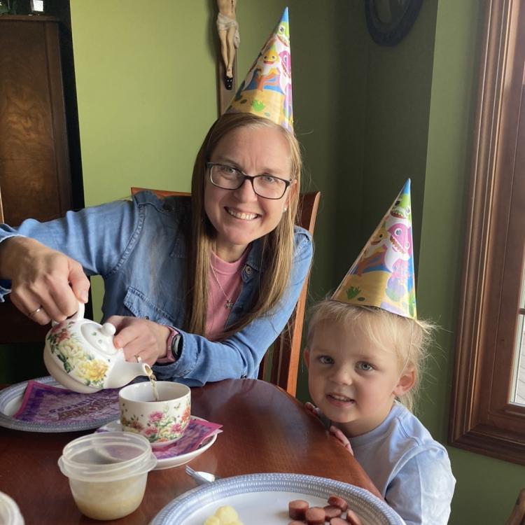 woman and little girl having tea, wearing party hats