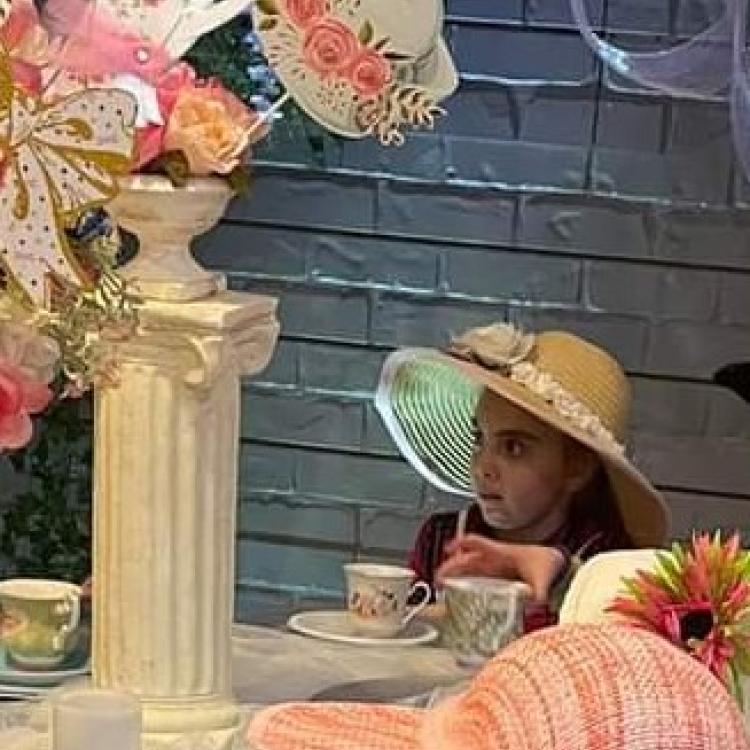 girl in pink sun hat enjoying a cup of tea