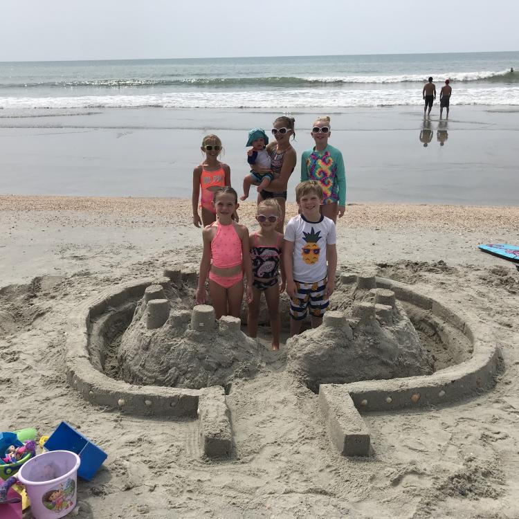 six kids and a baby in and around large sandcastle