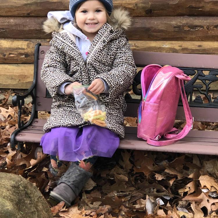 little girl in winter coat and hat on bench surrounded by leaves