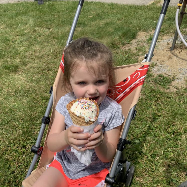 Little girl sits in stroller, holding big ice cream cone.