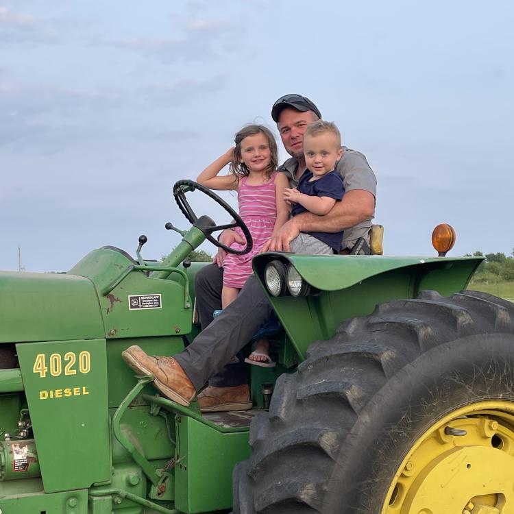 man on green tractor with small girl and boy