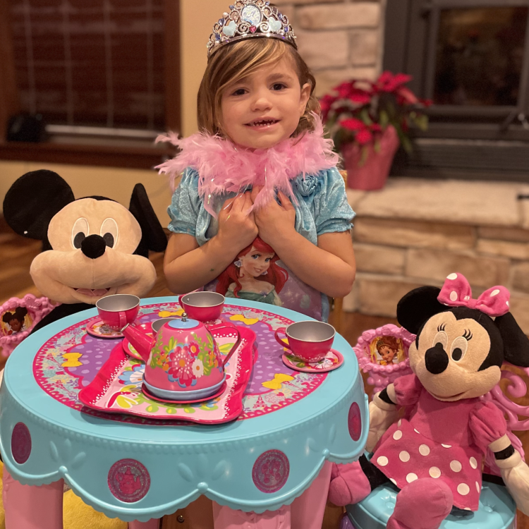 little girl in boa and tiara having tea with stuffed Mickey and Minnie Mouse