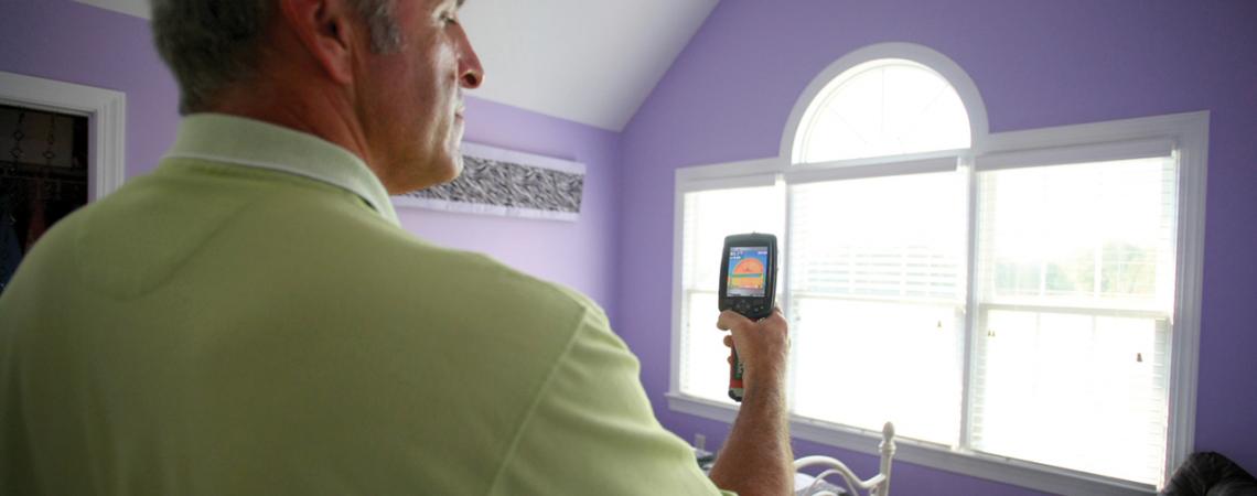 An energy auditor uses an infrared camera to look for areas around the window that are leaky or poorly insulated.