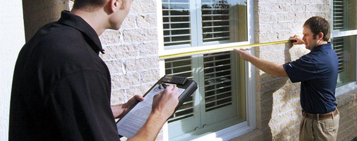 A man measures a window while another records the measurements.