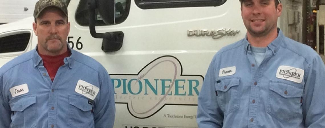 Lineworkers Jason Woods and Trevor Lavy smile for a picture beside a Pioneer Electric truck.