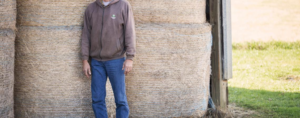 Roger Rhonemus poses for a picture next to a stack of haybales. 