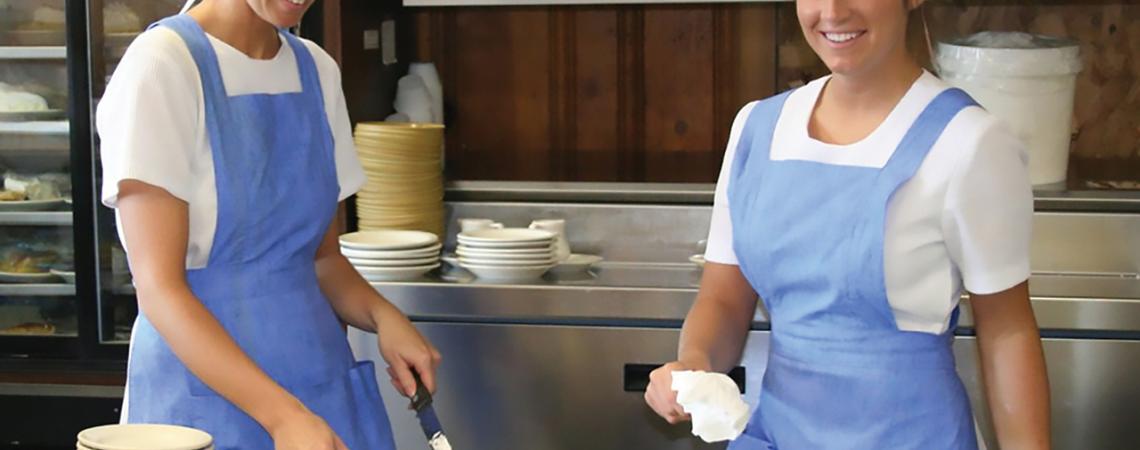 Two women making pies pose for a picture.