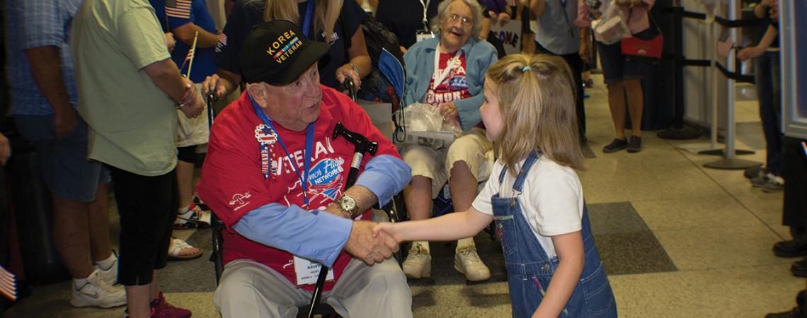 A young girl shakes the hand of a male veteran.