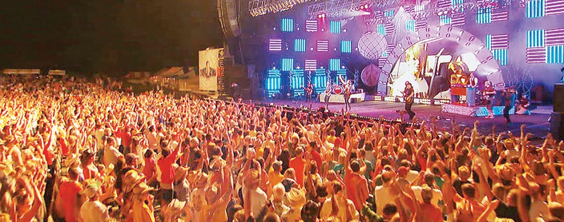 A large crowd celebrates and dances in front of a stage