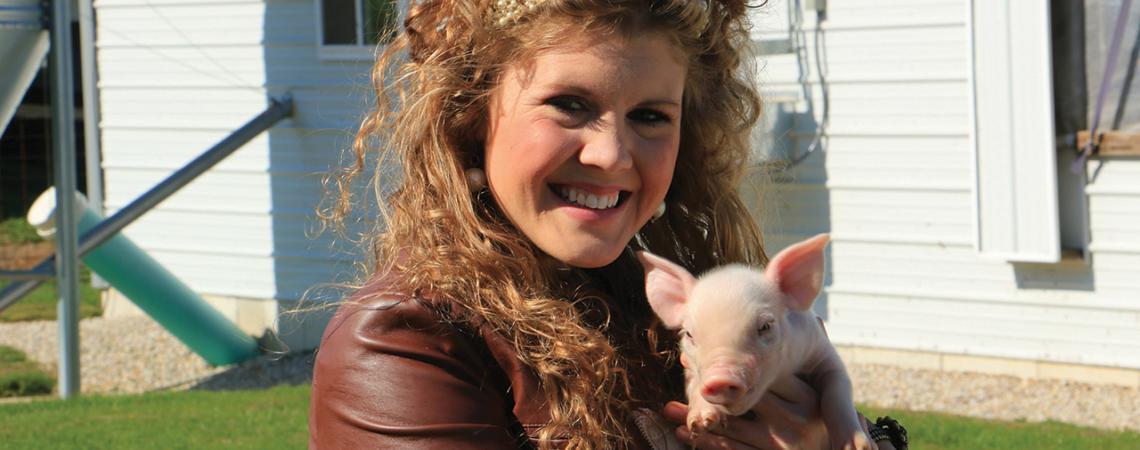 Lauren Schwab Eyre holds a baby pig and smiles for a picture.