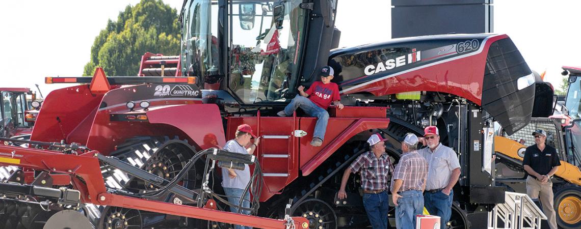 A few men stand around a giant red tractor while a child sits on the side of it.