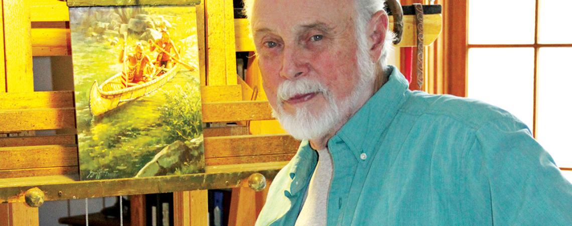 Robert Griffing looks into the camera as he sits next to a piece of his art depicting a canoe.