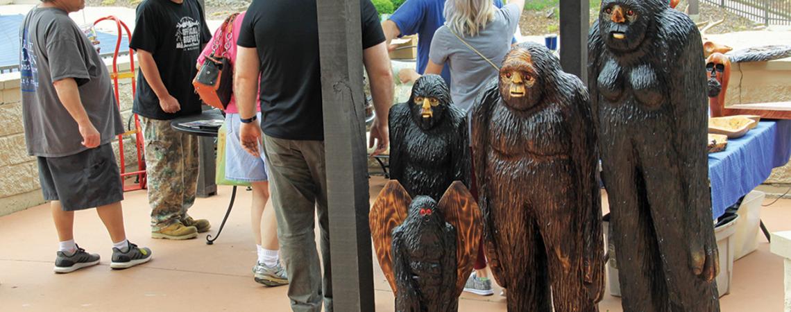 A group of people stand next to multiple statues of Bigfoot.