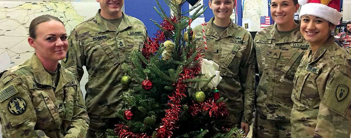 American Troops smile around a Christmas tree.