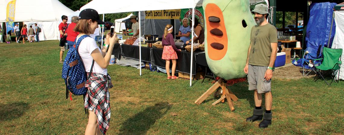 A girl takes a picture of someone next to a pawpaw mascot.-