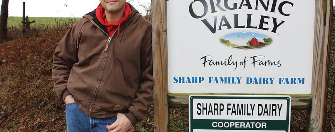 Kyle Sharp poses next to his family farm's sign.